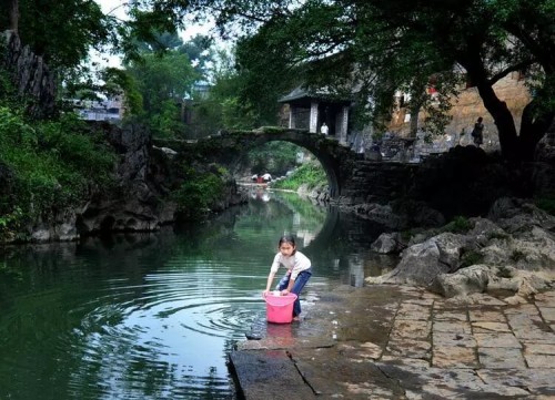 姚黄古镇，石拱桥下清流穿过，小女孩溪间提水暮然回首张望瞬间。